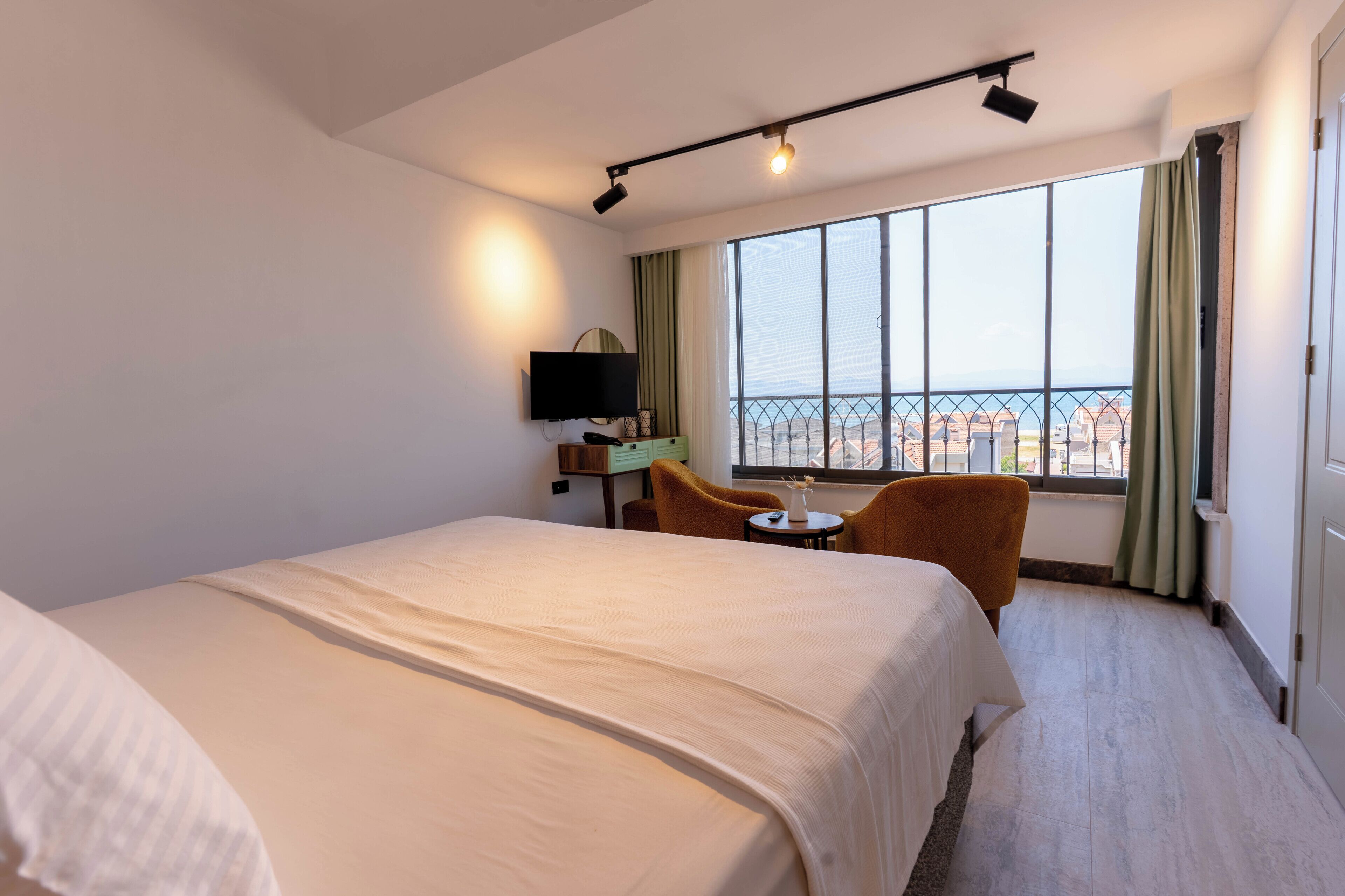 A hotel room with a large bed, a desk with a TV, a chair, and a window with a view of buildings.