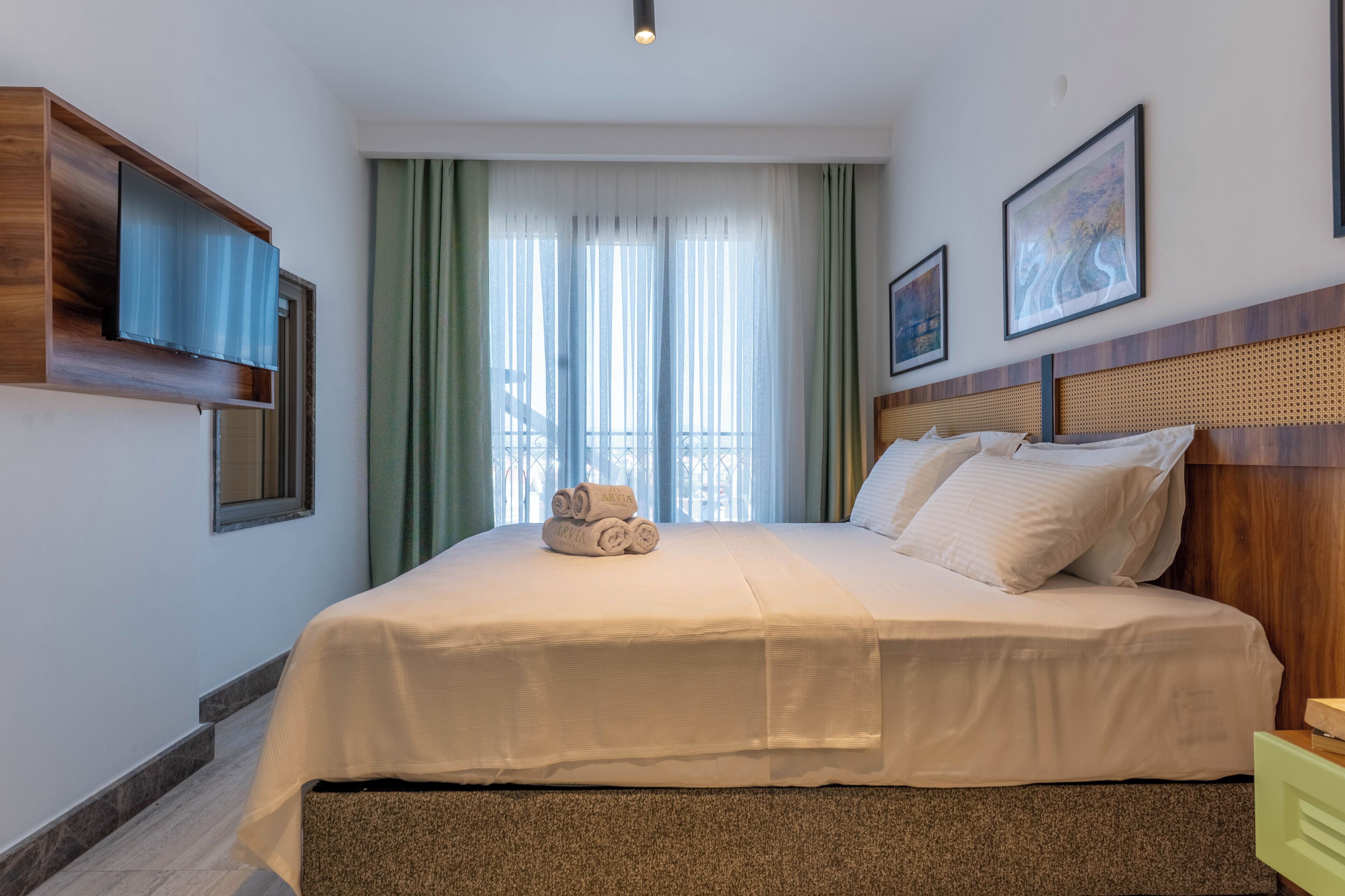 A hotel room with a large bed, a flat-screen TV mounted on the wall, and two framed artworks above the bed.