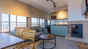 A modern living room with a sofa, chairs, a dining table, and a kitchen area with a microwave. - ARVIA SUITES (Altinova)