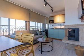 A modern living room with a sofa, chairs, a dining table, and a kitchen area with a microwave. - ARVIA SUITES (Altinova)