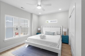 Ein Schlafzimmer mit Bett, Deckenventilator, Fenster und Nachttisch mit Lampe.