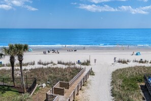 Ein Strand mit einer Holzpromenade, einer Palme und einem Zelt.