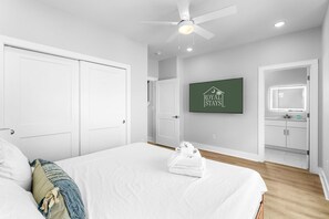 A hotel room with a bed, a ceiling fan, a mounted TV, and a bathroom with a mirror and cabinets. - Swell House 2.5 Blocks to Ocean Pet Friendly (Myrtle Beach)