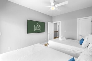 Quarto de hotel com duas camas, um ventilador de teto, um quadro na parede e uma porta que dá para uma varanda.