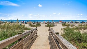 Een houten looppad naar een strand met parasols en mensen.