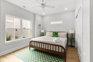 A bedroom with a bed, two bedside lamps, a ceiling fan, a window, and a green patterned rug. - The Social House-Pet Friendly-2.5 Blocks to Beach (Myrtle Beach)