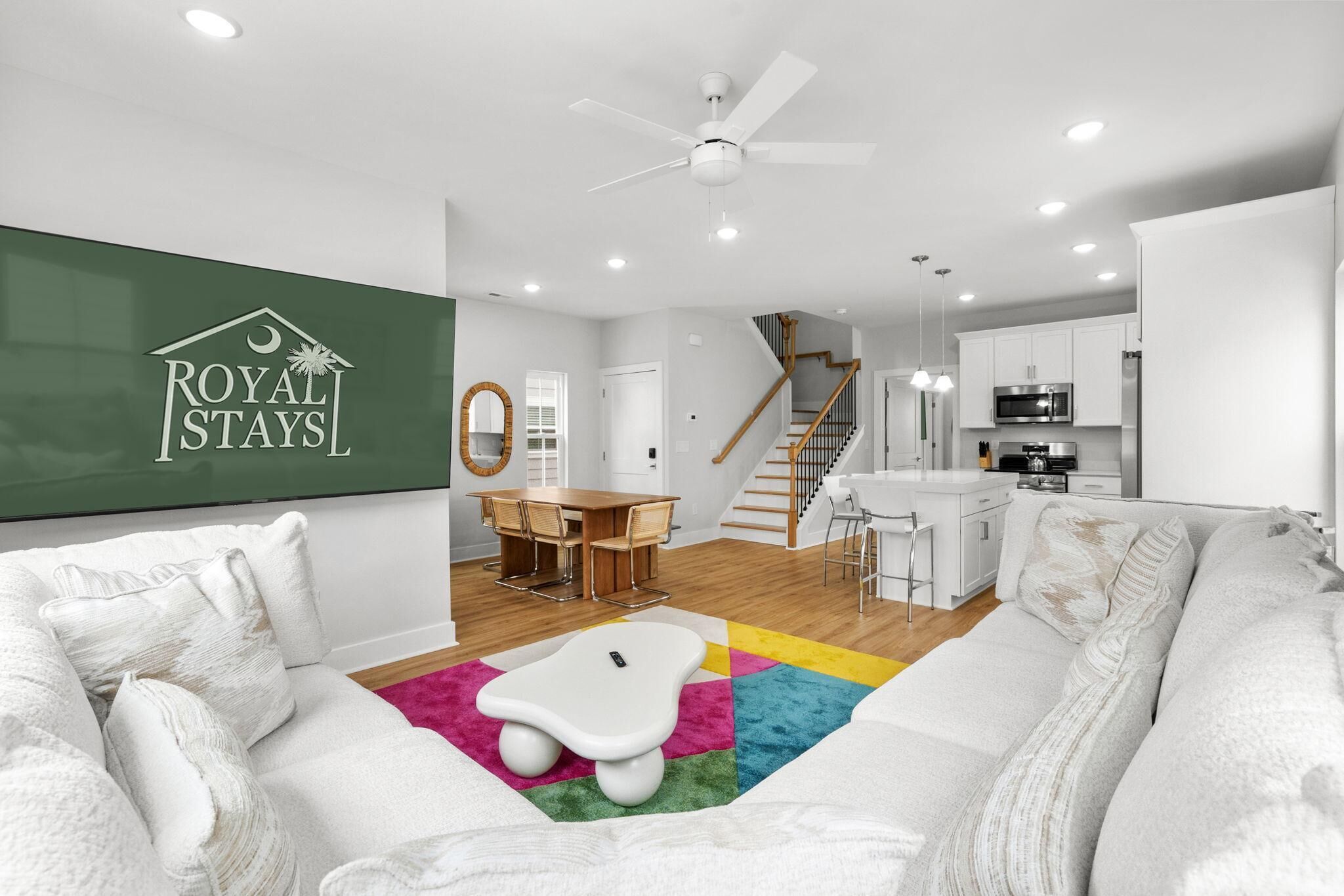 A modern living room with a sofa, a coffee table, and a dining area with a table and chairs. There is a kitchen area with a microwave and cabinets.