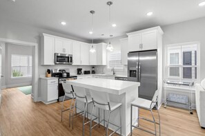 A modern kitchen with white cabinetry, stainless steel appliances, and a central island with bar stools. - The Social House-Pet Friendly-2.5 Blocks to Beach (Myrtle Beach)