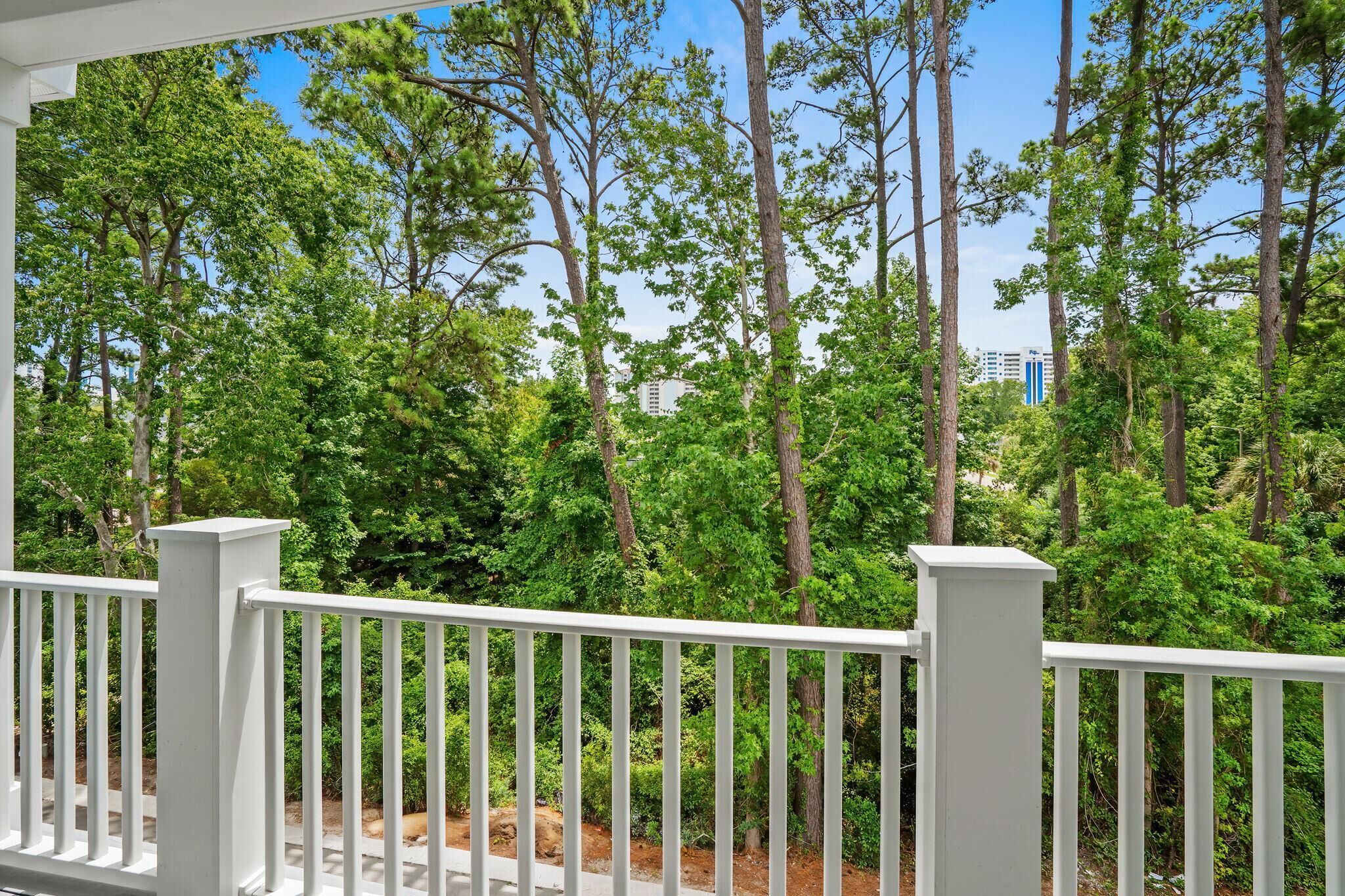 Une balustrade de balcon blanche, avec vue sur une forêt dense et un bâtiment en arrière-plan.