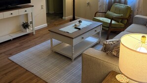 A living room with a flat-screen TV, a coffee table, a sofa, a lamp, and a chair.