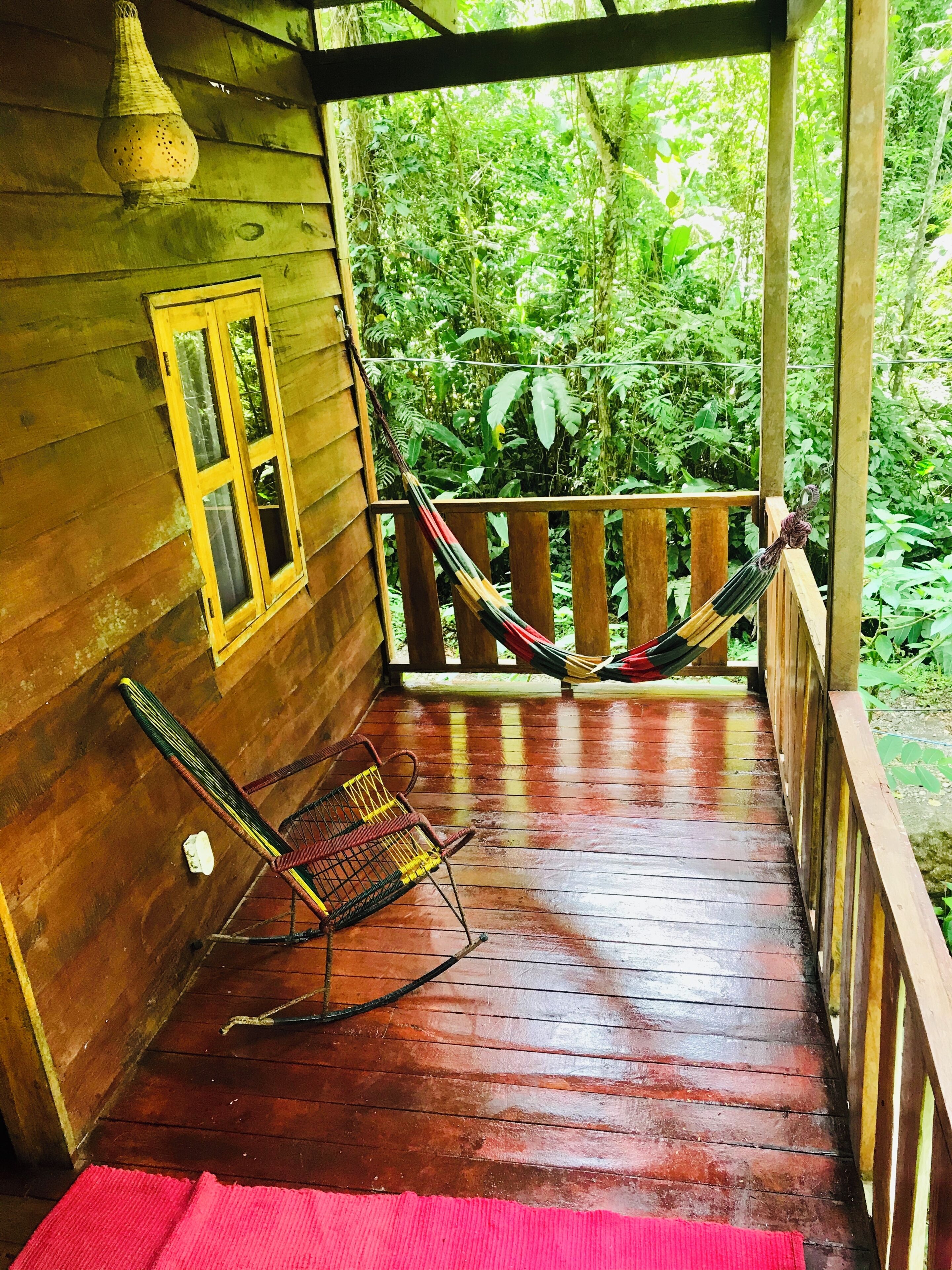 A wooden porch with a hammock, a chair, and a window.