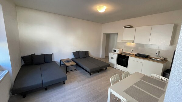 A compact living space with a sofa, a small table, a kitchenette, and a microwave.