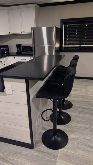 A kitchen with a black countertop, stainless steel appliances, white cabinets, and a window with blinds.