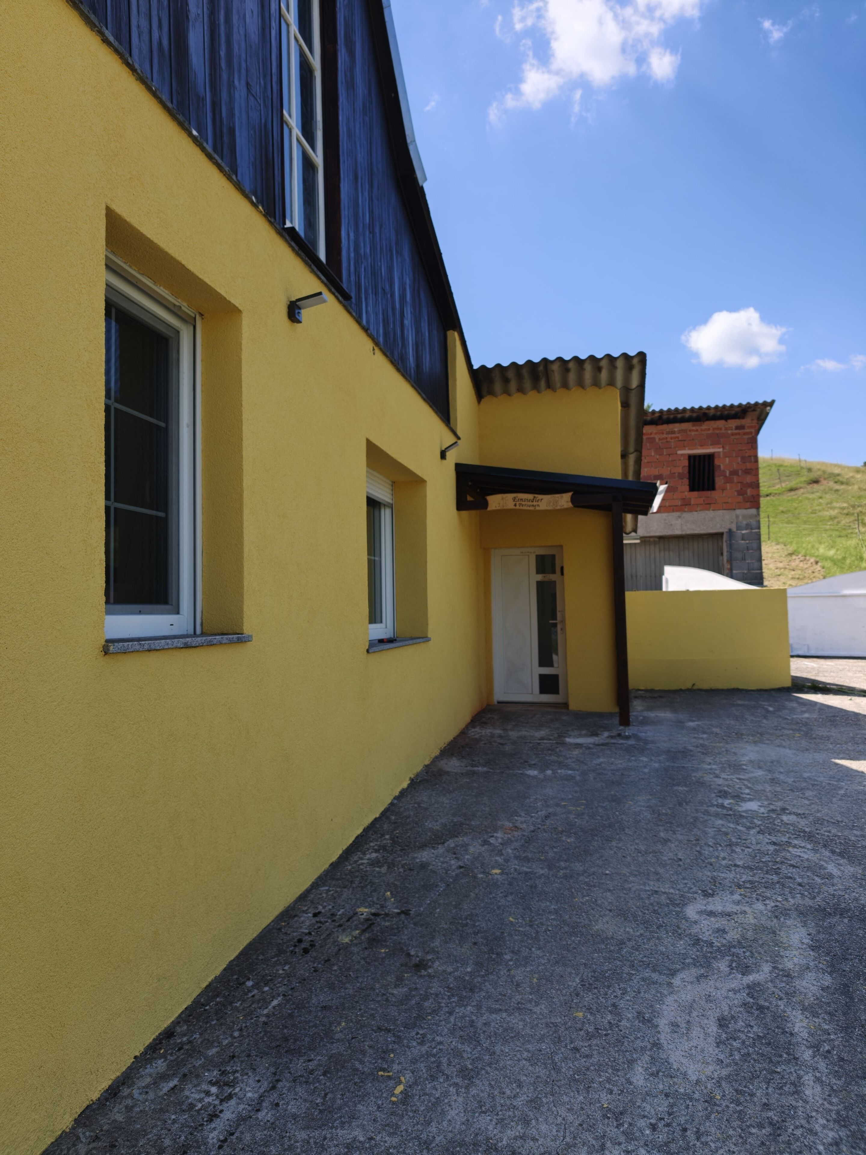 A yellow building with a small door and windows, a gravel driveway, and a clear blue sky.