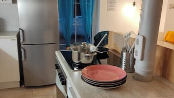 A kitchen with a stainless steel refrigerator, a stove, and a sink. There are plates stacked on the counter and a pot on the stove.