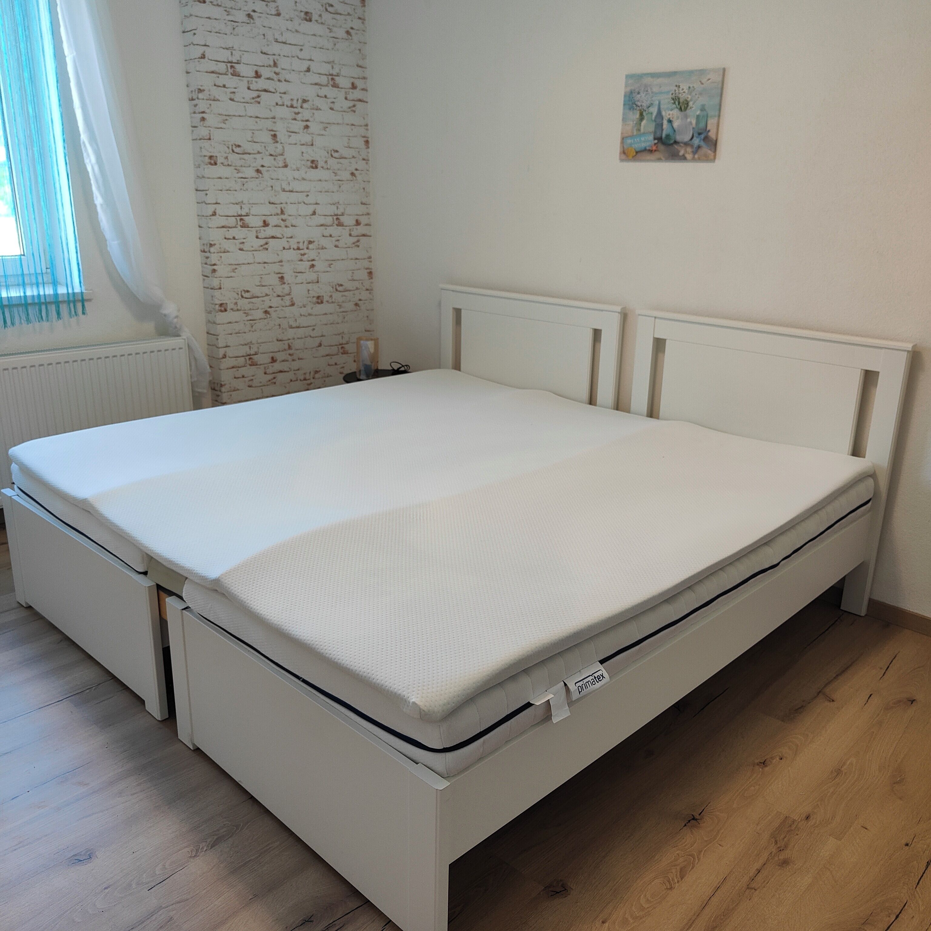 Una cama blanca con etiqueta del colchón, cabecera blanca y suelo de madera.
