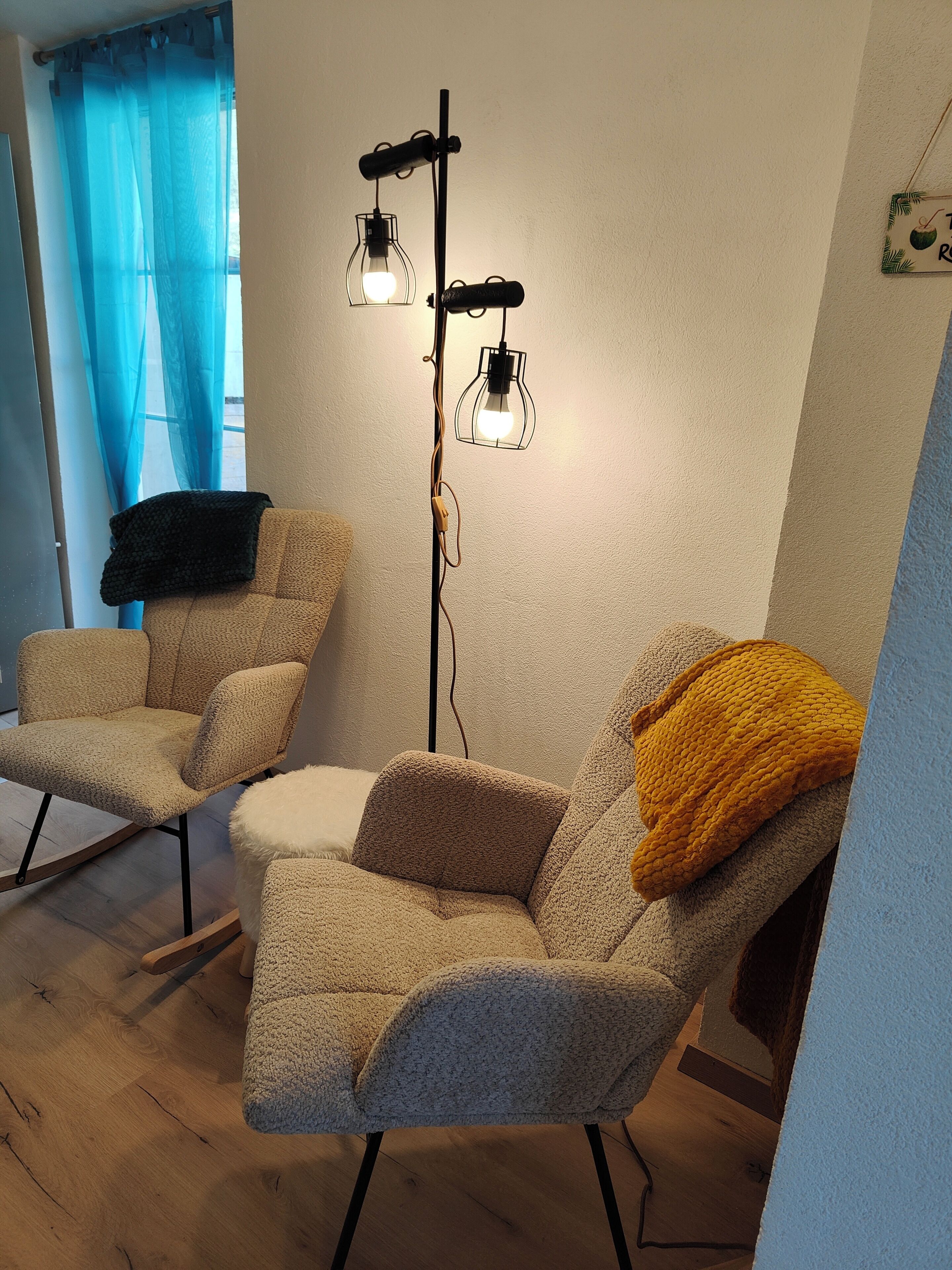 A room with two armchairs, a floor lamp, and a window with blue curtains.