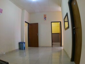 A hallway with a blue trash bin, a wooden door, and a yellow door leading to another room.