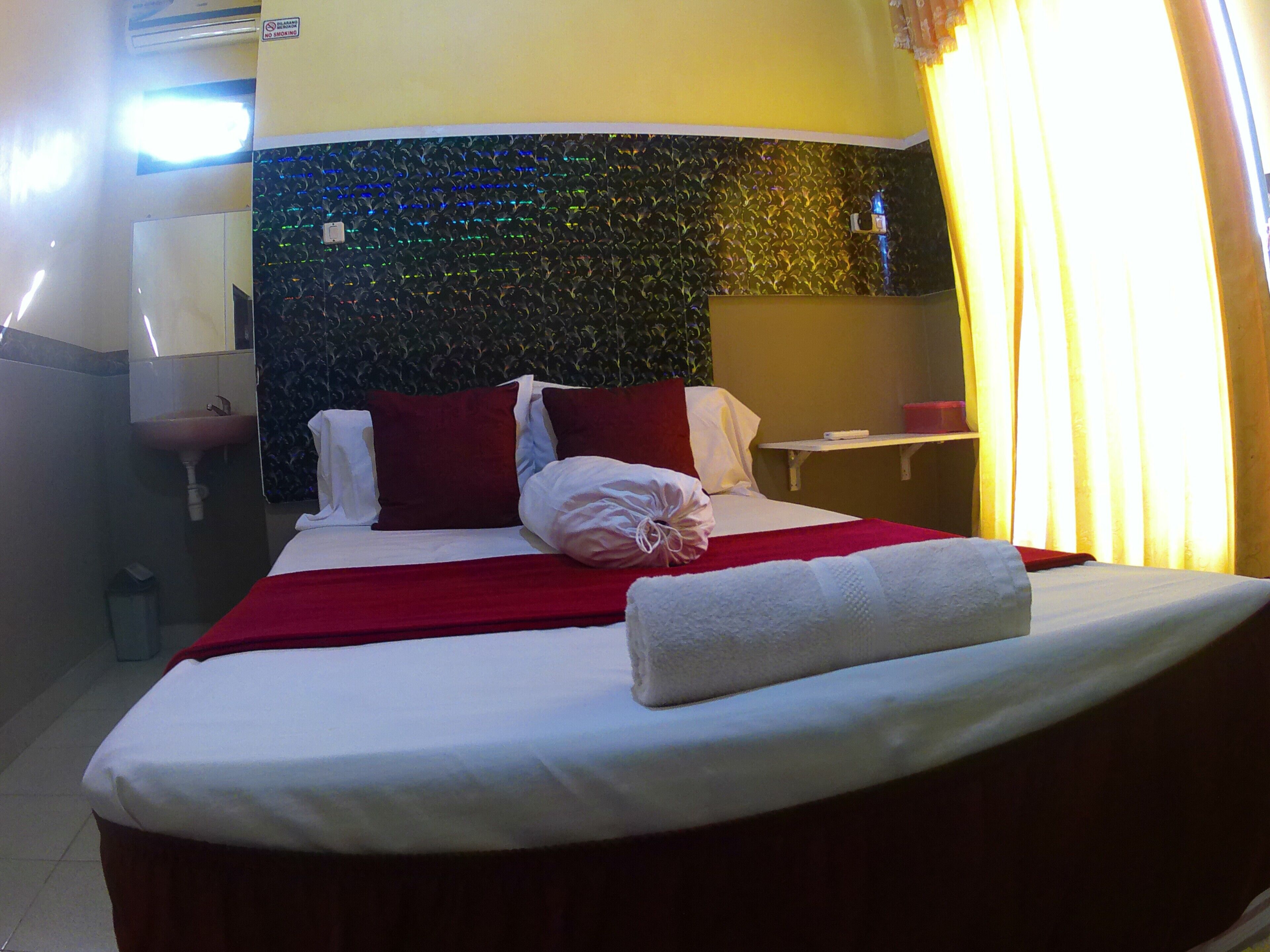 Quarto de hotel com cama, mesa de cabeceira, espelho, pia e área de chuveiro.