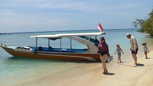 A beach scene with a boat, clear skies, and people walking along the shore.