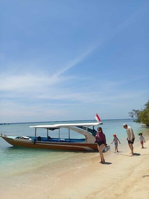 A beach scene with a boat, clear skies, and people walking along the shore.
