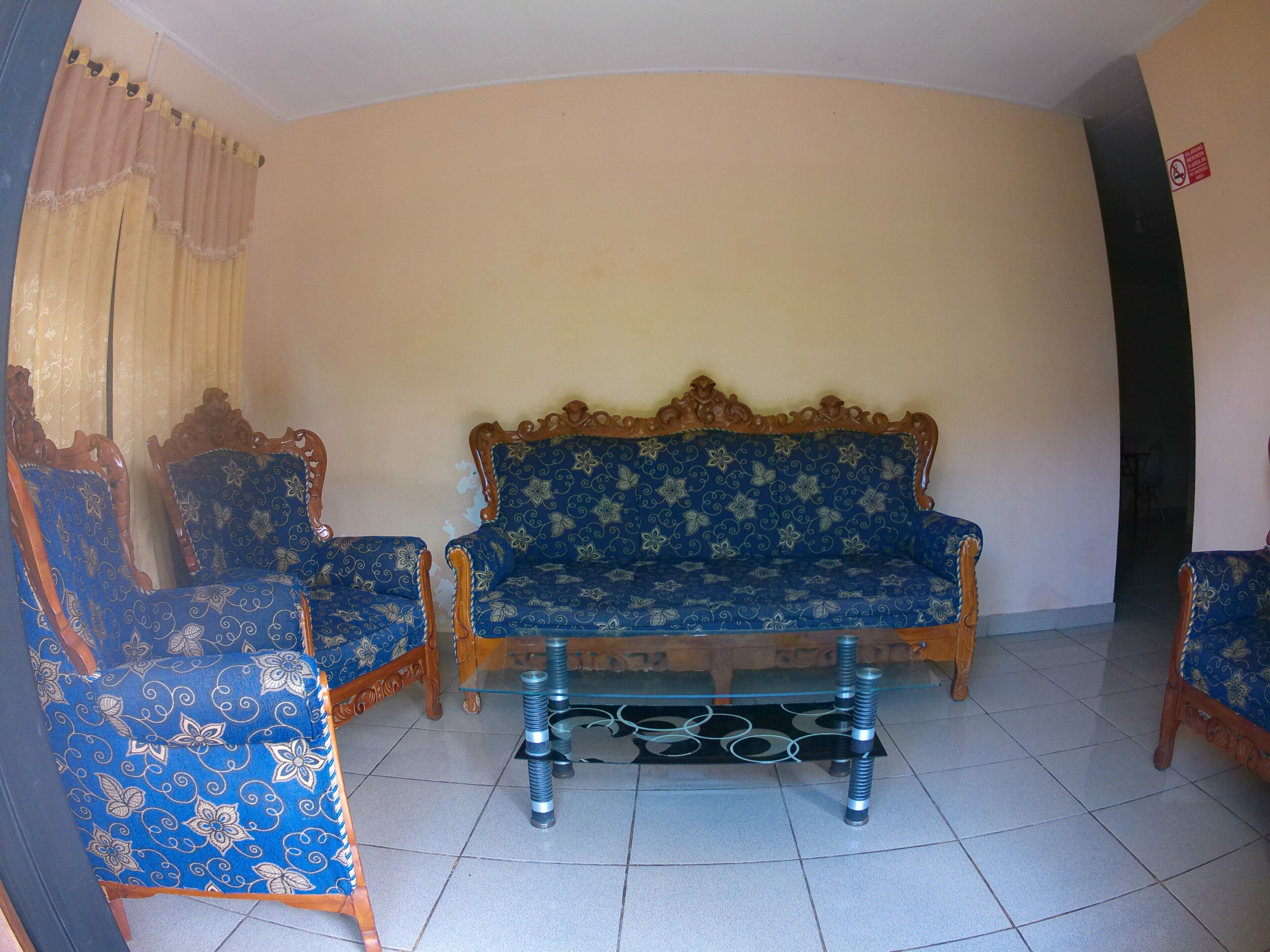 Un salón con un sofá, dos sillones, una mesa de centro de vidrio y una cortina.