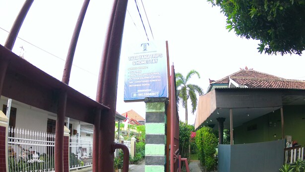 A gated entrance with a signboard for Taba Yama Tours & Homestay, listing services like tour trips and motorbike rental.