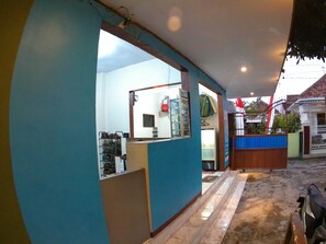 Un pasillo con pared azul, suelo de baldosas y una reja metálica que da a una casa.