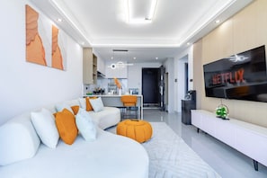 Una sala de estar moderna con un sofá seccional, un reposapiés y un televisor de pantalla plana montado en la pared.