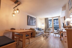 A cozy living room with a wooden dining table, sofa, and chairs, a painting on the wall, and a window with curtains. - VAL D'ISERE, in the heart of the village, 2-room apartment with a terrace and parking (Val-d'Isère)