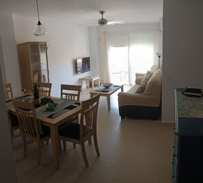 A living room with a sofa, a dining table with chairs, a television, and a ceiling fan. - Beautiful two-bedroom, two-bathroom apartment with a pool in the center of Nerja (Nerja)