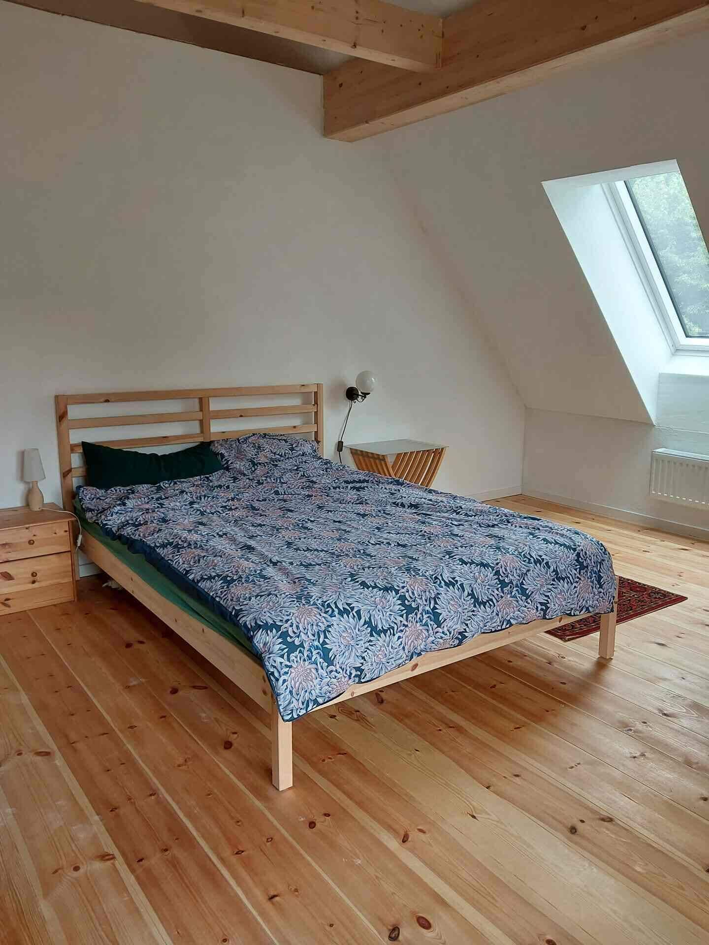 Une chambre à coucher avec un lit en bois, une petite table de chevet, une lampe et une fenêtre.