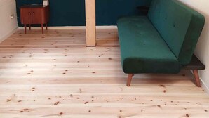 Et værelse med skråvægge, en grøn sofa, et lille træskab og en hængende lyspære.