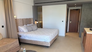 A modern hotel room with a large bed, a small round table with a vase, a sofa, and a wooden wardrobe. - Stella Elite Suites (Zakynthos)