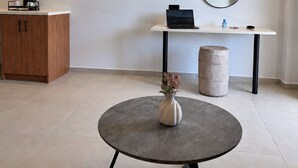 A modern room with a round table, a flat-screen TV mounted on the wall, a small desk with a laptop, a wooden cabinet, and a round ottoman. - Stella Elite Suites (Zakynthos)