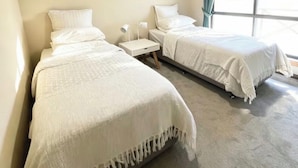 Une chambre d’hôtel avec deux lits, un ventilateur de plafond, une fenêtre avec des rideaux et une table de chevet avec une lampe.