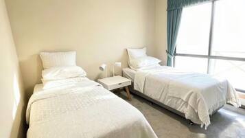 A hotel room with two beds, a ceiling fan, a window with curtains, and a nightstand with a lamp.