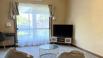 A living room with a ceiling fan, a flat-screen TV, two bean bags, a glass coffee table, and a window with curtains.