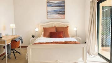 A bedroom with a bed, desk, chair, and a window with curtains.
