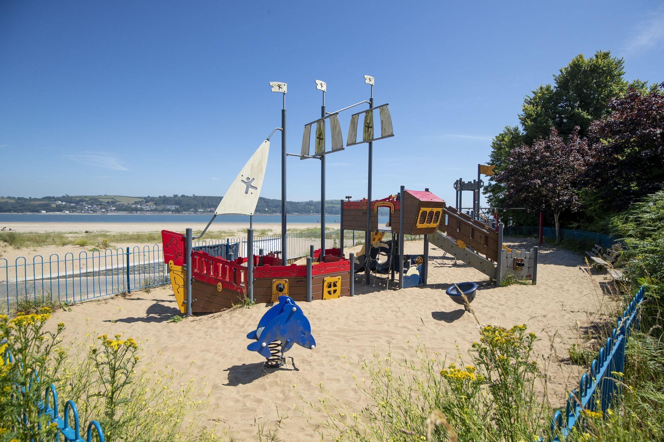 Une aire de jeux de plage avec une structure ludique sur le thème d’un navire, comprenant des toboggans et des zones d’escalade.
