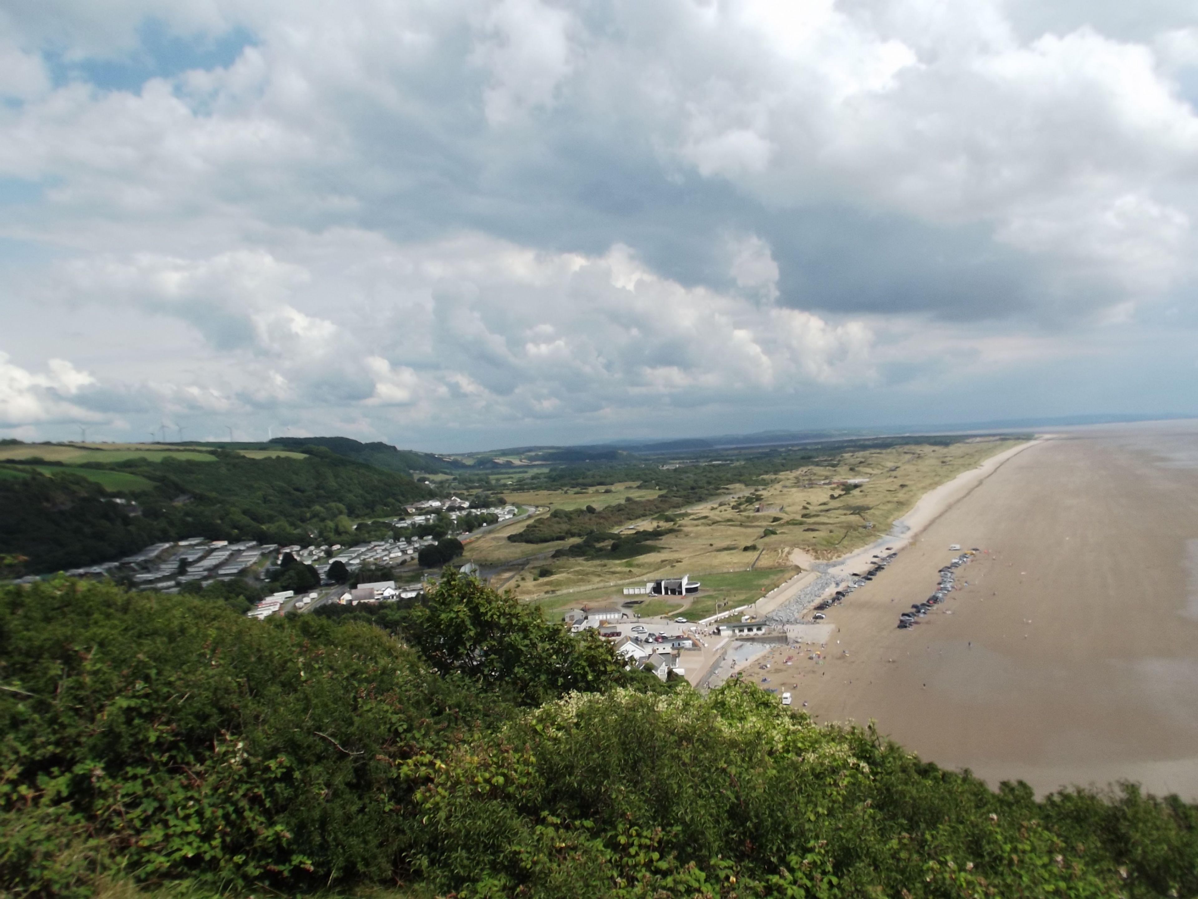 Un paysage côtier avec une plage, des collines douces et une vue lointaine sur une ville.