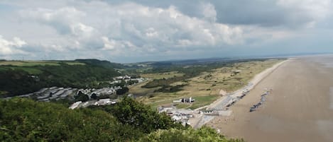A coastal landscape with a beach, rolling hills, and a distant view of a town.