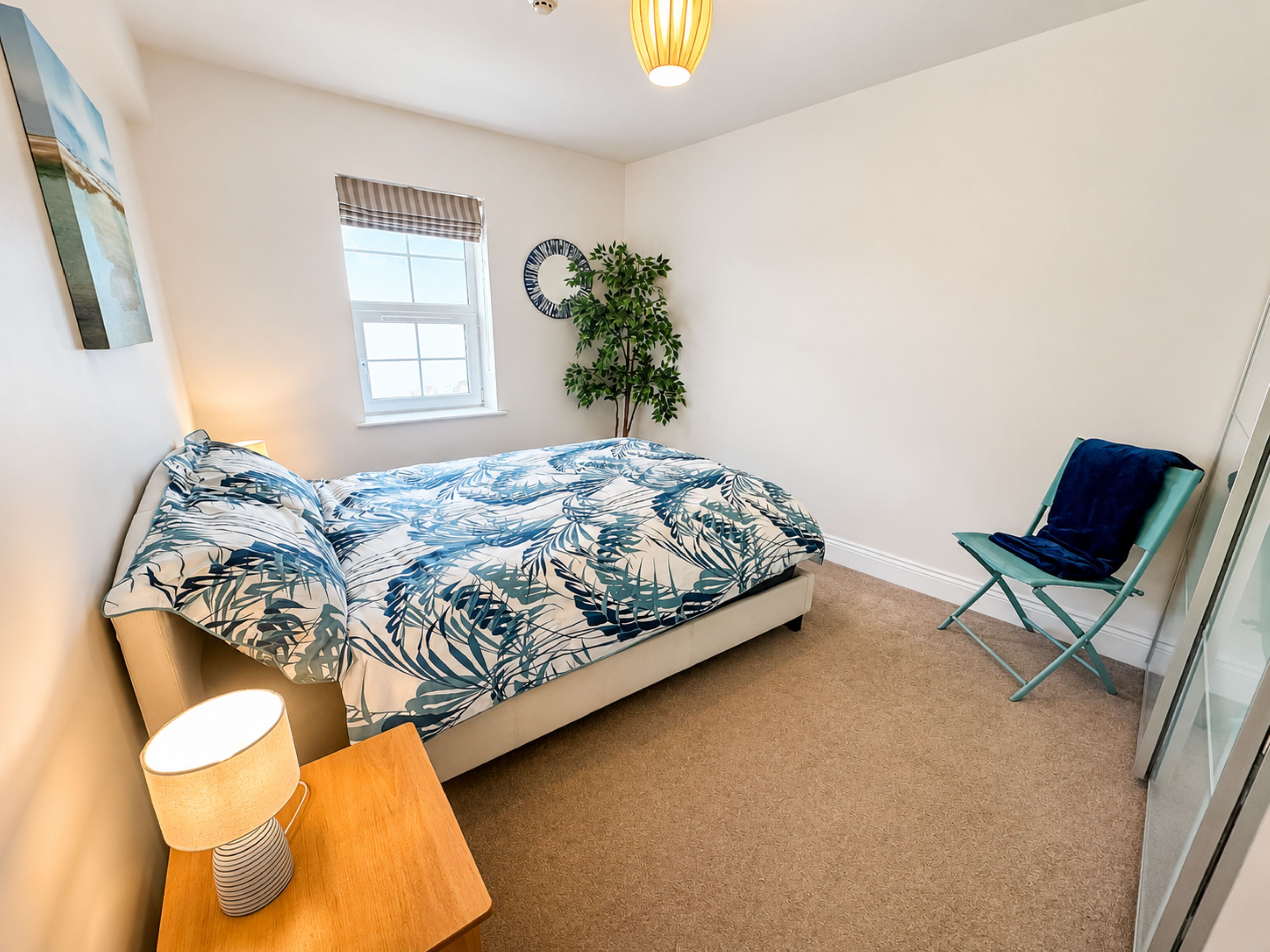 A bedroom with a bed, a chair, a lamp, a window, and a plant.