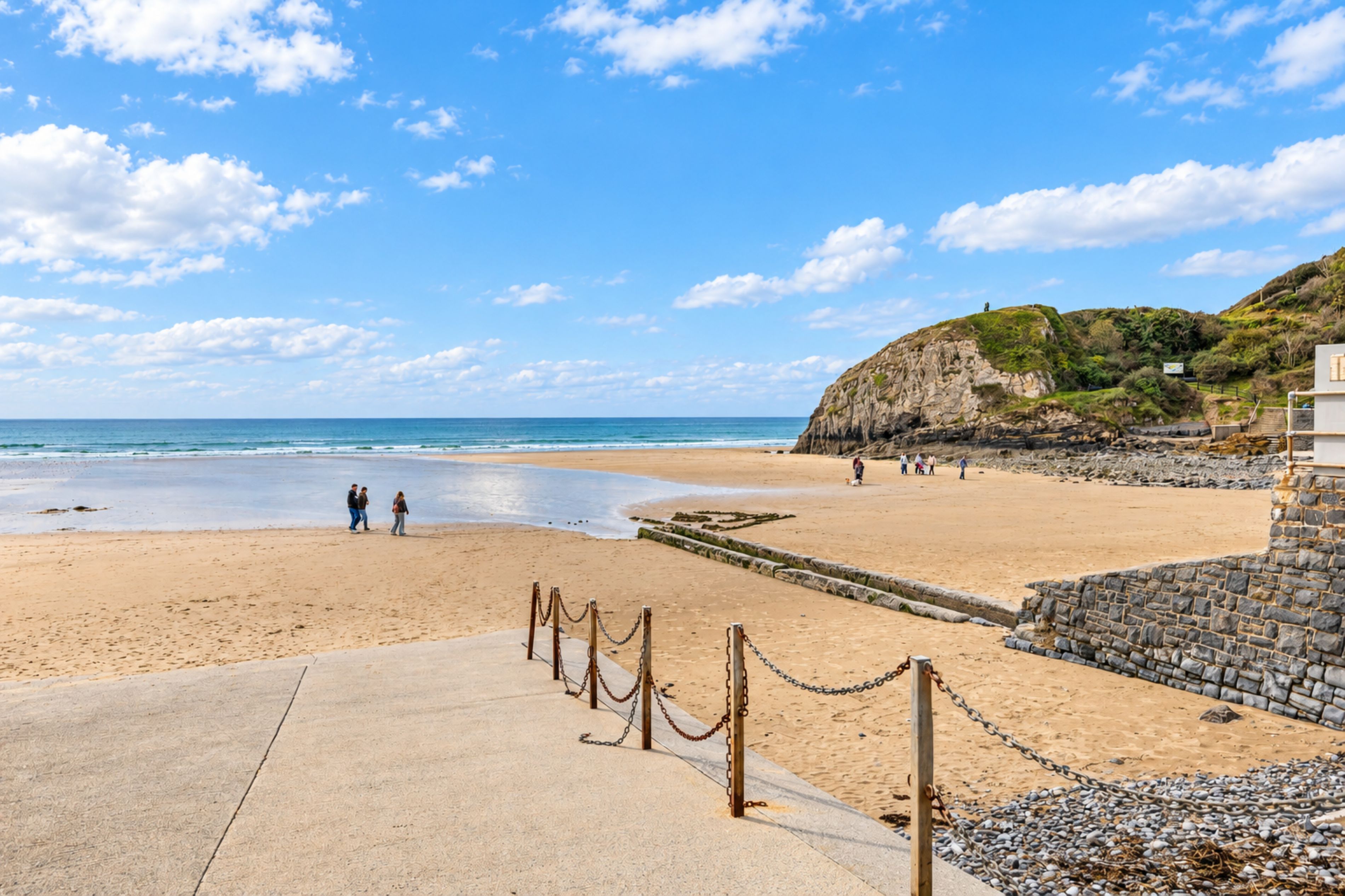 A beach with a stone wall and a chain barrier.