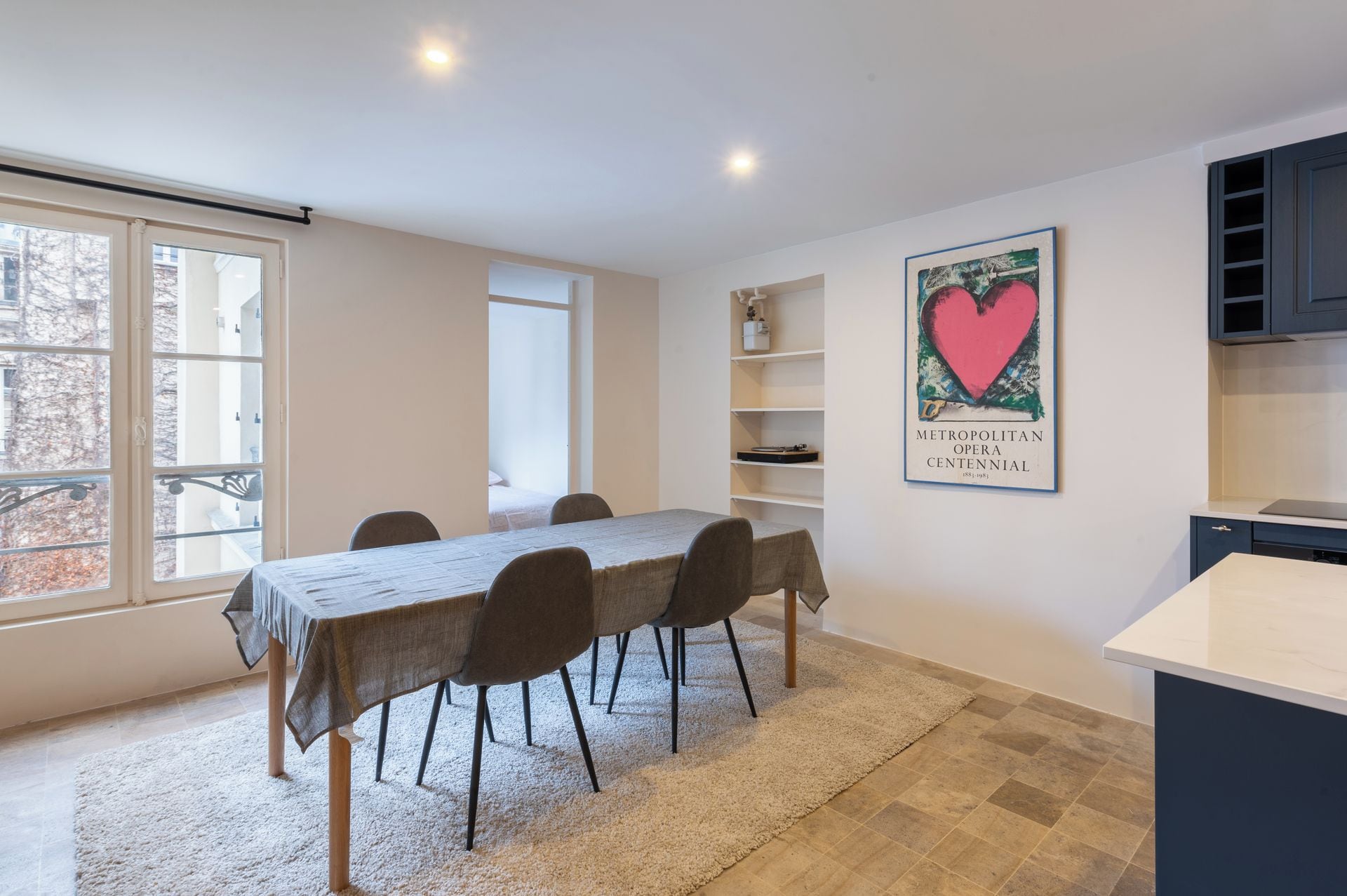 A dining area with a table, chairs, a rug, a kitchen area with cabinets, and a framed picture on the wall.