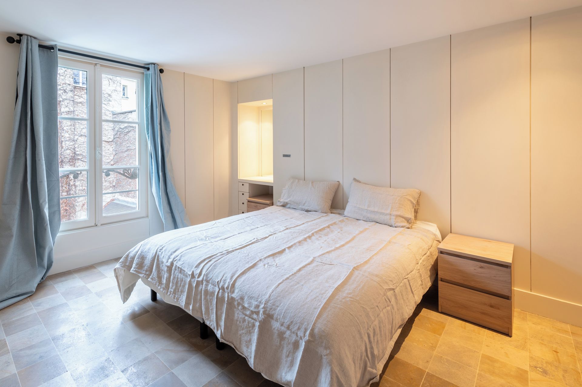 A bedroom with a bed, bedside tables, and a window with curtains.