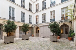 Ein Innenhof mit Kopfsteinpflaster, Kübelbepflanzung und einem Gebäude mit mehreren Fenstern und Balkonen.