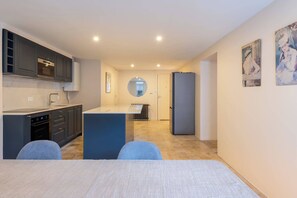 Eine moderne Küche mit einer zentralen Kochinsel, einem Essbereich mit Tisch und einer Wohnfläche mit Sofa.