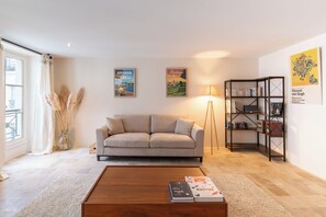 Ein Wohnzimmer mit einer Couch, einem Couchtisch, einem Bücherregal und zwei gerahmten Bildern an der Wand.