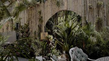 Un jardín privado con cerramiento de bambú, diversas plantas tropicales y mobiliario exterior.